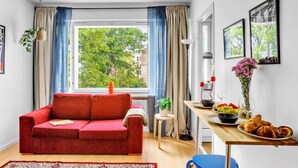 Una sala de estar acogedora con un sofá rojo, una mesita con un florero y una ventana con cortinas azules.