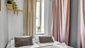 Una cama bien tendida con dos almohadas, una mesita de noche con una toalla y una ventana con cortinas.