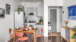 Una cocina moderna con armarios blancos, un refrigerador de acero inoxidable y una zona de comedor con una mesa de madera y sillas rojas.