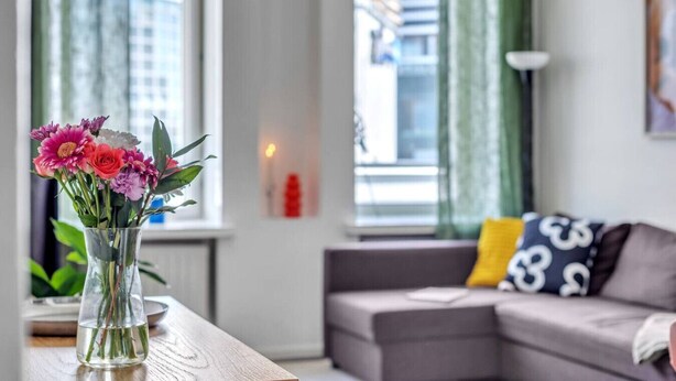 Una sala de estar con un sofá, un jarrón de flores y una ventana con cortinas.