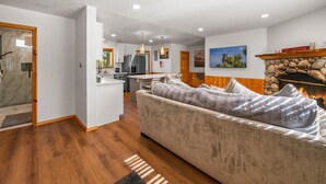 A modern living room with a sofa, a fireplace, and a kitchen area in the background. - Log Cabin Dream - Log Cabin, Walk to Lake, Fireplace, Deck, BBQ (Big Bear Lake)