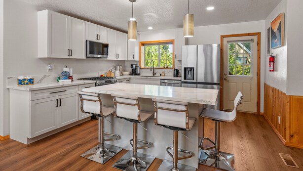 A modern kitchen with white cabinets, stainless steel appliances, and a central island with bar stools. - Log Cabin Dream - Log Cabin, Walk to Lake, Fireplace, Deck, BBQ (Big Bear Lake)