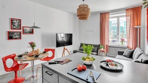 Et moderne køkken med en central ø, røde stole, et spisebord og et fjernsyn monteret på væggen.