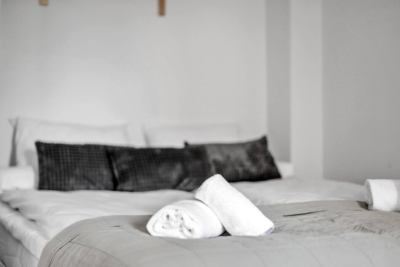 Una cama bien hecha con sábanas blancas y una toalla enrollada al lado.