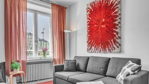En moderne stue med en grå sofa, røde gardiner, en hvid radiator og et abstrakt rødt billede på væggen.