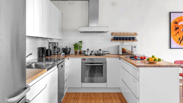 Een moderne keuken met witte kastjes, roestvrijstalen apparatuur, een houten aanrecht en een magnetron.