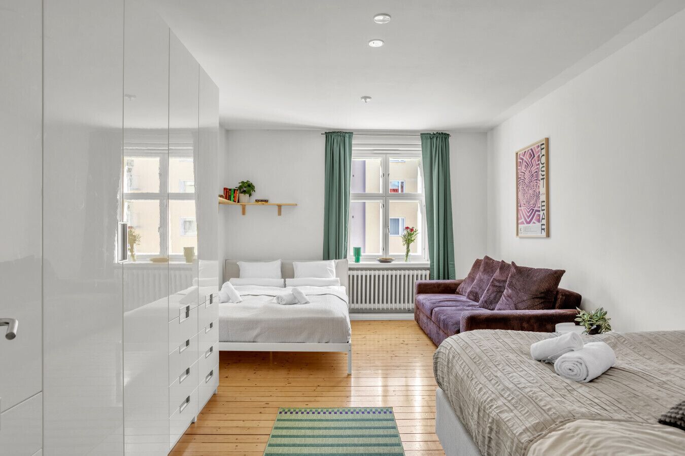Ein modernes Schlafzimmer mit Bett, einer Couch, einem Heizkörper und einem Fenster mit Vorhängen.