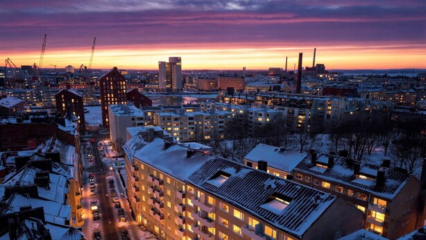 A high-rise hotel with multiple floors, a central courtyard, and a view of the surrounding cityscape during twilight. - Sunny Views | Design District | Balcony | WiFi (Helsinki)