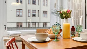A breakfast setting with a table, a vase with flowers, a glass of orange juice, and a croissant. - Sunny Views | Design District | Balcony | WiFi (Helsinki)