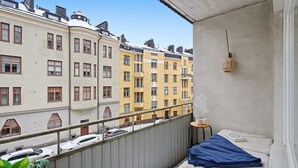 A balcony with a view of adjacent buildings, a small table with a cup, and a hanging light fixture. - Sunny Views | Design District | Balcony | WiFi (Helsinki)