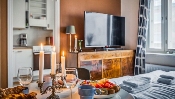A hotel room with a bed, a dining table with candles, a fruit bowl, and a television on a wooden cabinet. - Vibrant & Central w Netflix, WiFi, 200m tram/bus (Helsinki)