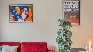 A living room with a red sofa, a dining table with chairs, a potted plant, and two framed artworks on the wall. - Vibrant & Central w Netflix, WiFi, 200m tram/bus (Helsinki)