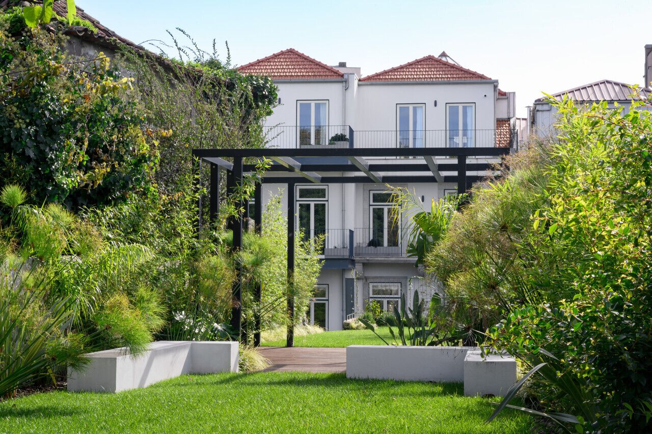 Ein modernes, zweistöckiges Haus mit Balkon, umgeben von üppiger Vegetation und einem gepflegten Rasen.