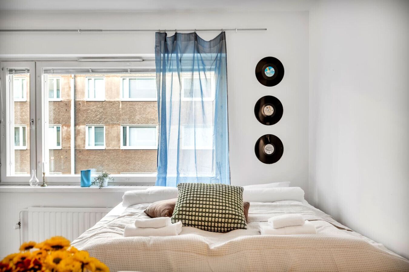 Une chambre à coucher avec un lit, une fenêtre avec des rideaux et trois disques vinyle accrochés au mur.