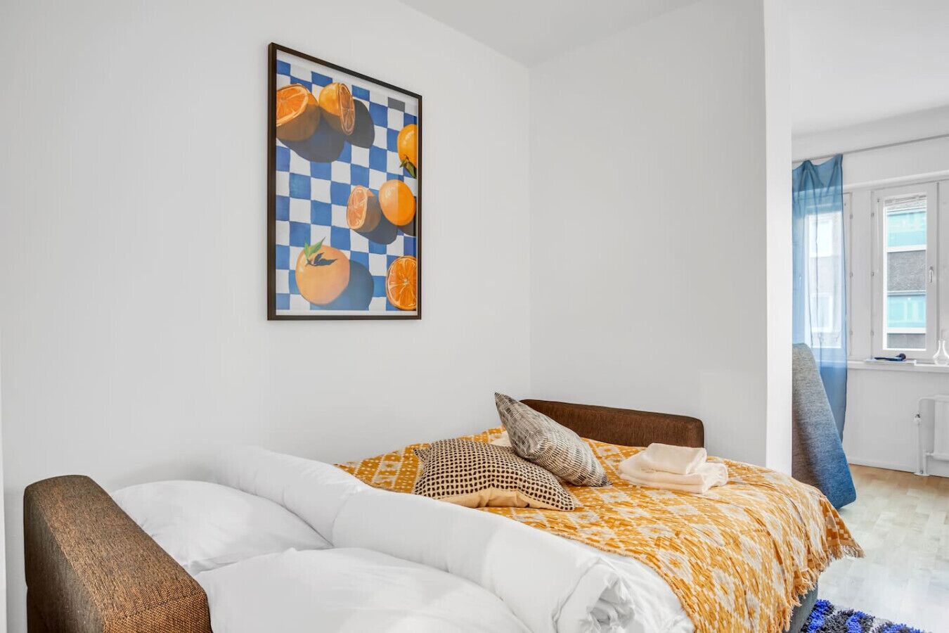 A bedroom with a bed, a chair, a window with curtains, and a framed artwork on the wall.