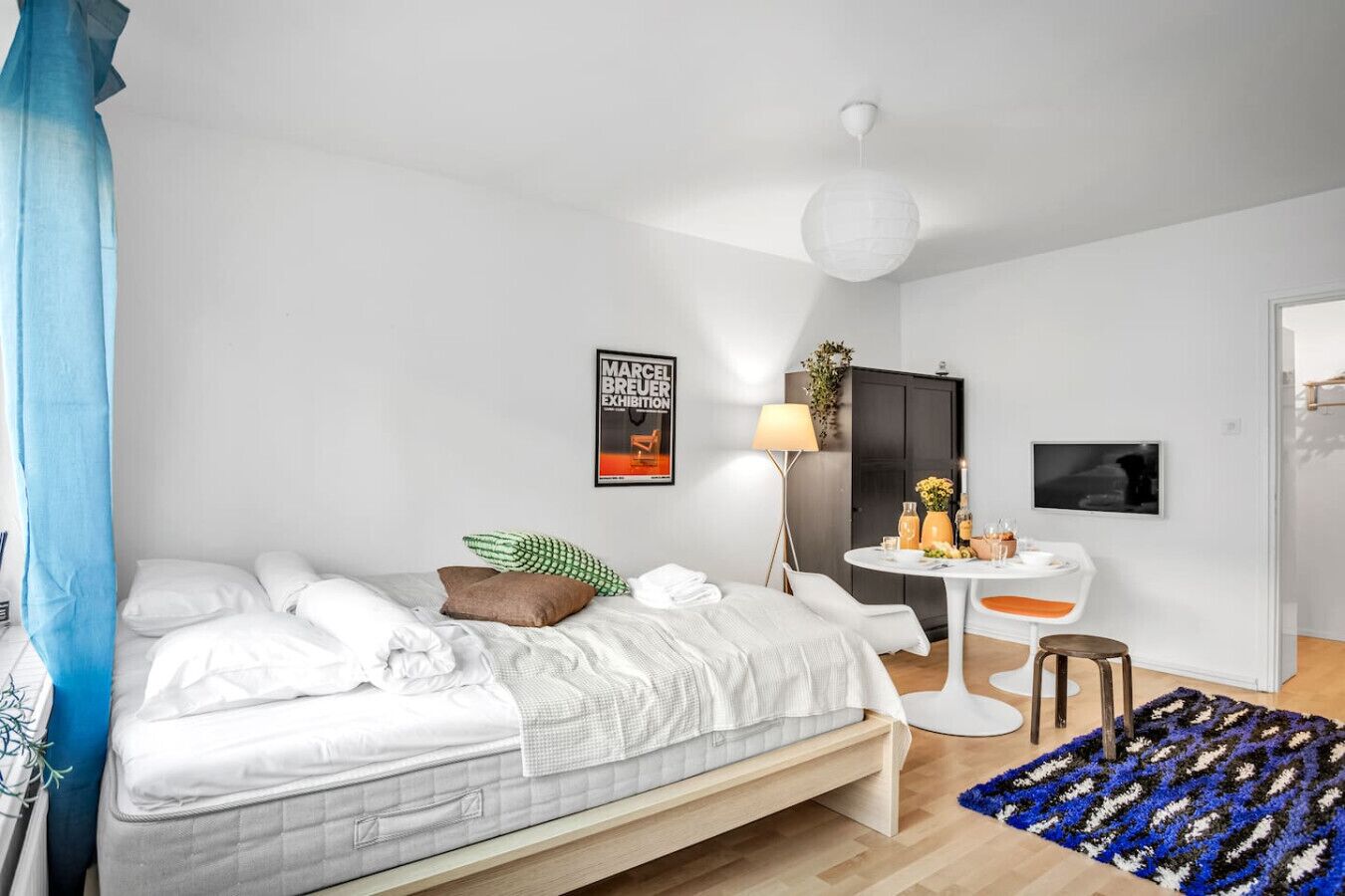 Een moderne slaapkamer met een bed, nachtkastje, lamp en een poster aan de muur.
