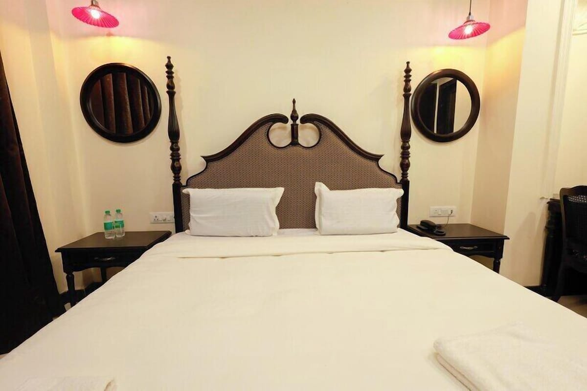 A hotel room with a large bed, two bedside tables, a round mirror, and two wall-mounted lamps.
