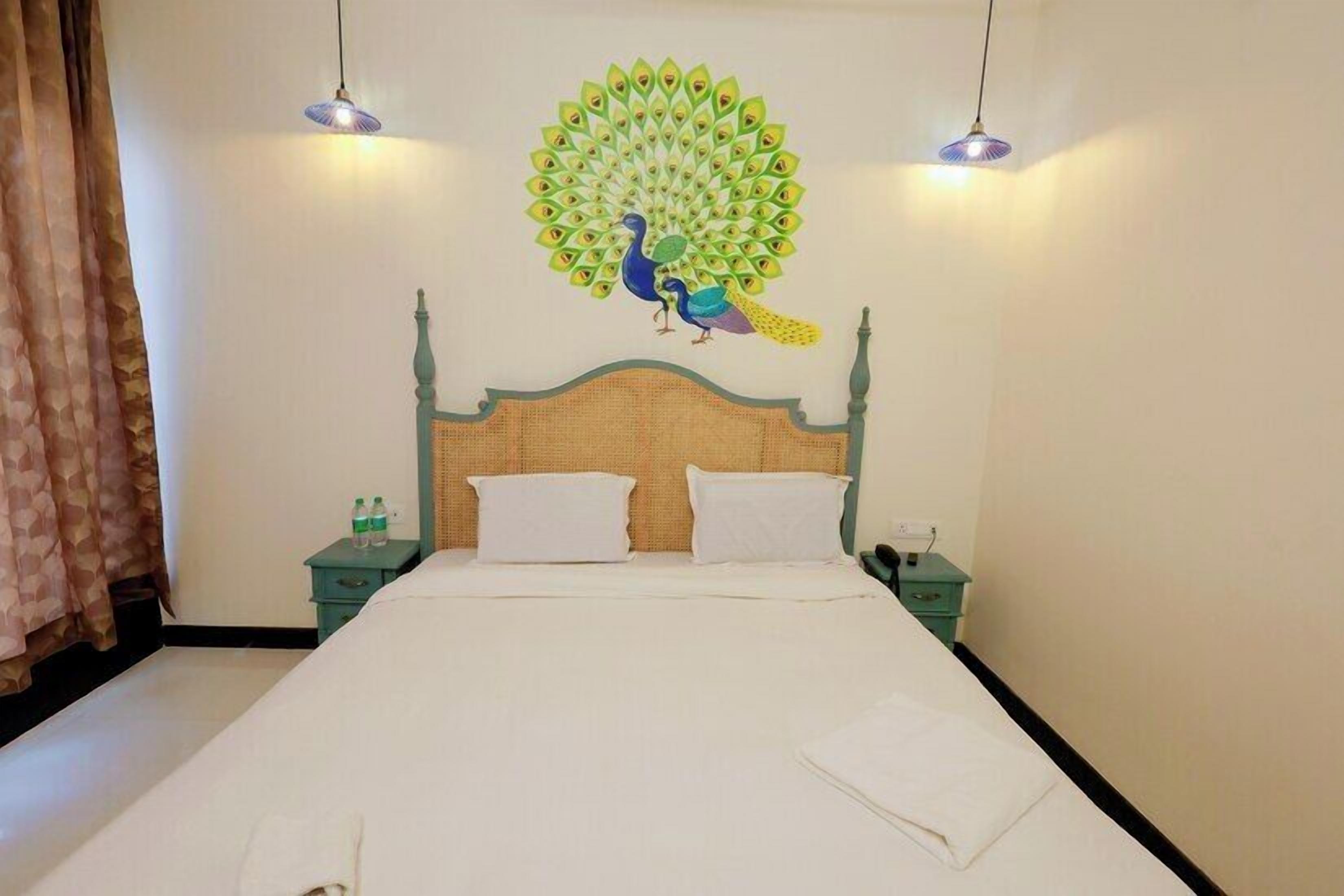 A room with a bed, two bedside tables, a wall mural of a peacock, and two hanging lamps.