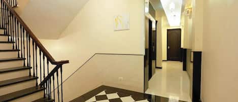 Un vestíbulo de hotel con piso a cuadros blanco y negro, una escalera con barandales negros y una pared lisa con una pequeña obra de arte.