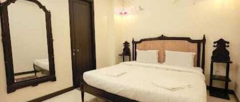 A bedroom with a single bed, a mirror, a door, and a small table.