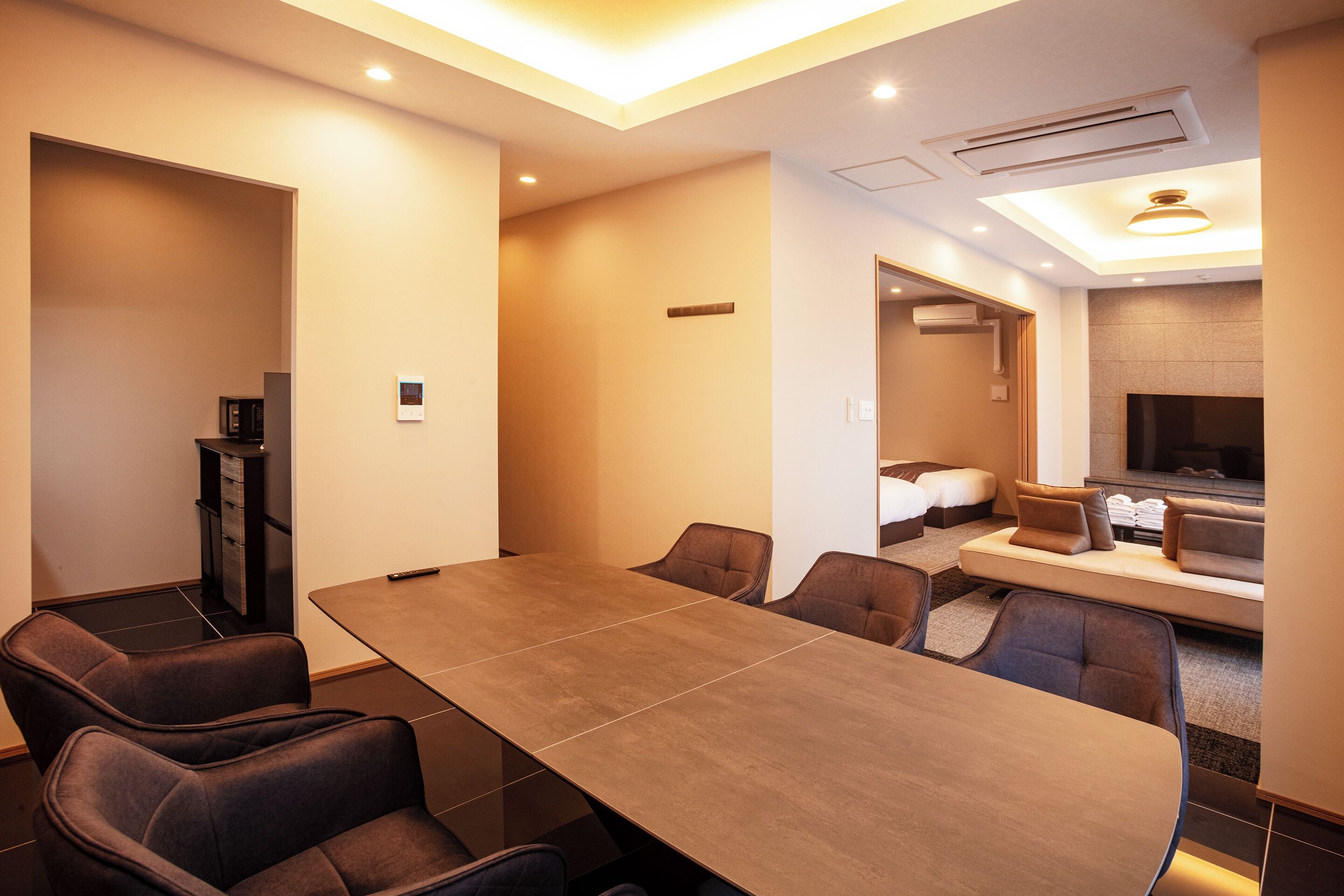 A modern hotel room with a large dining table, comfortable seating, a television, and a sofa.