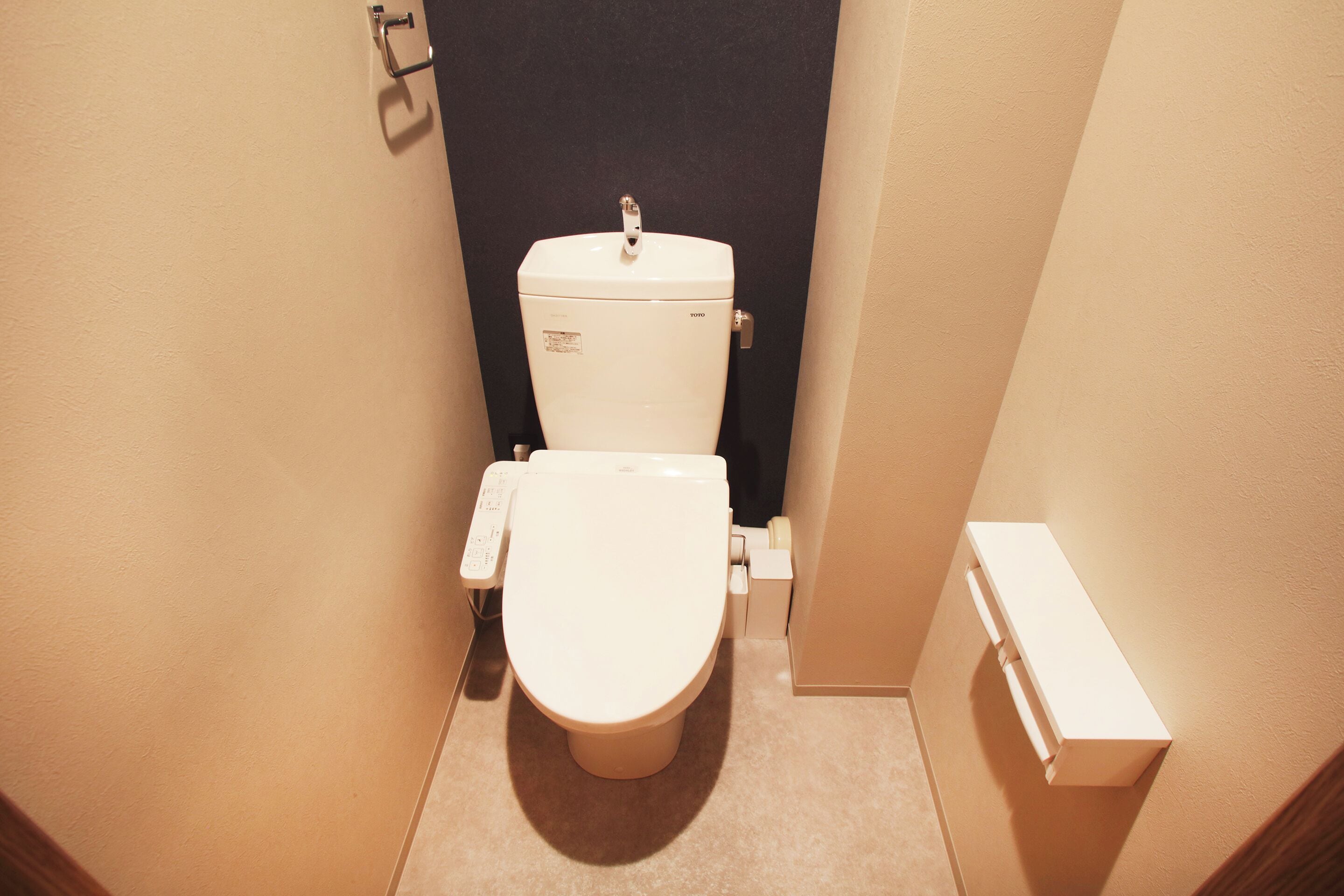 Un baño pequeño y funcional con un inodoro blanco, un secador de manos en la pared y un mueble de almacenamiento blanco.