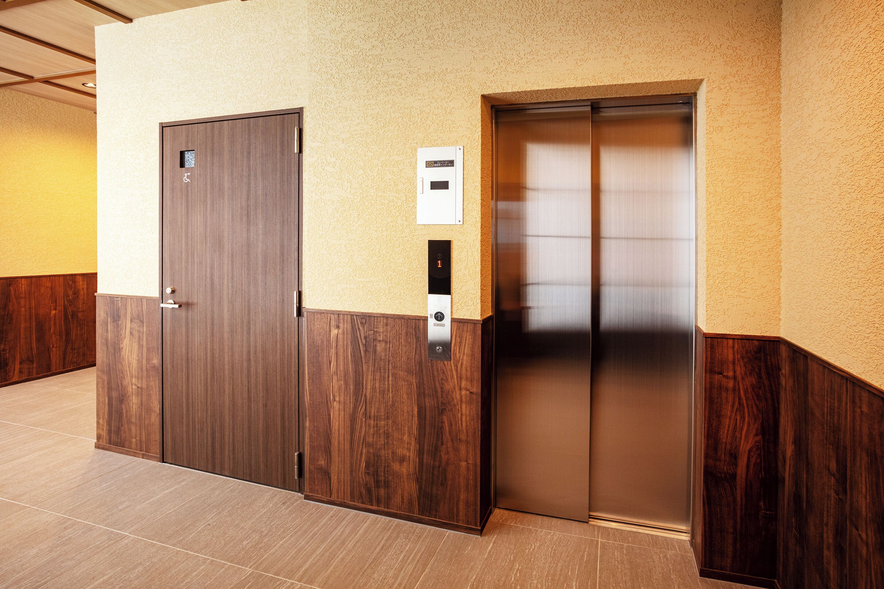 An elevator and a door in a hotel lobby with a textured wall and wooden paneling.