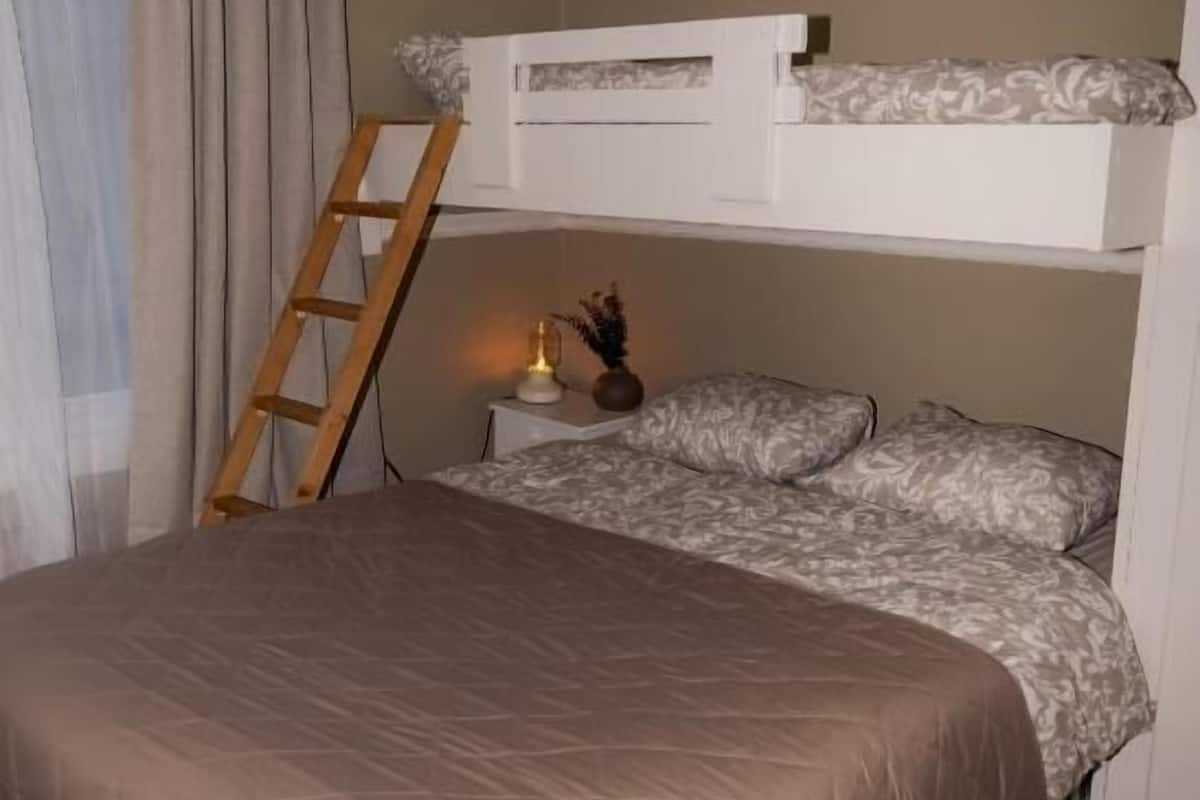 A bedroom with a bunk bed, a ladder, a bedside table with a lamp, and a window with curtains.