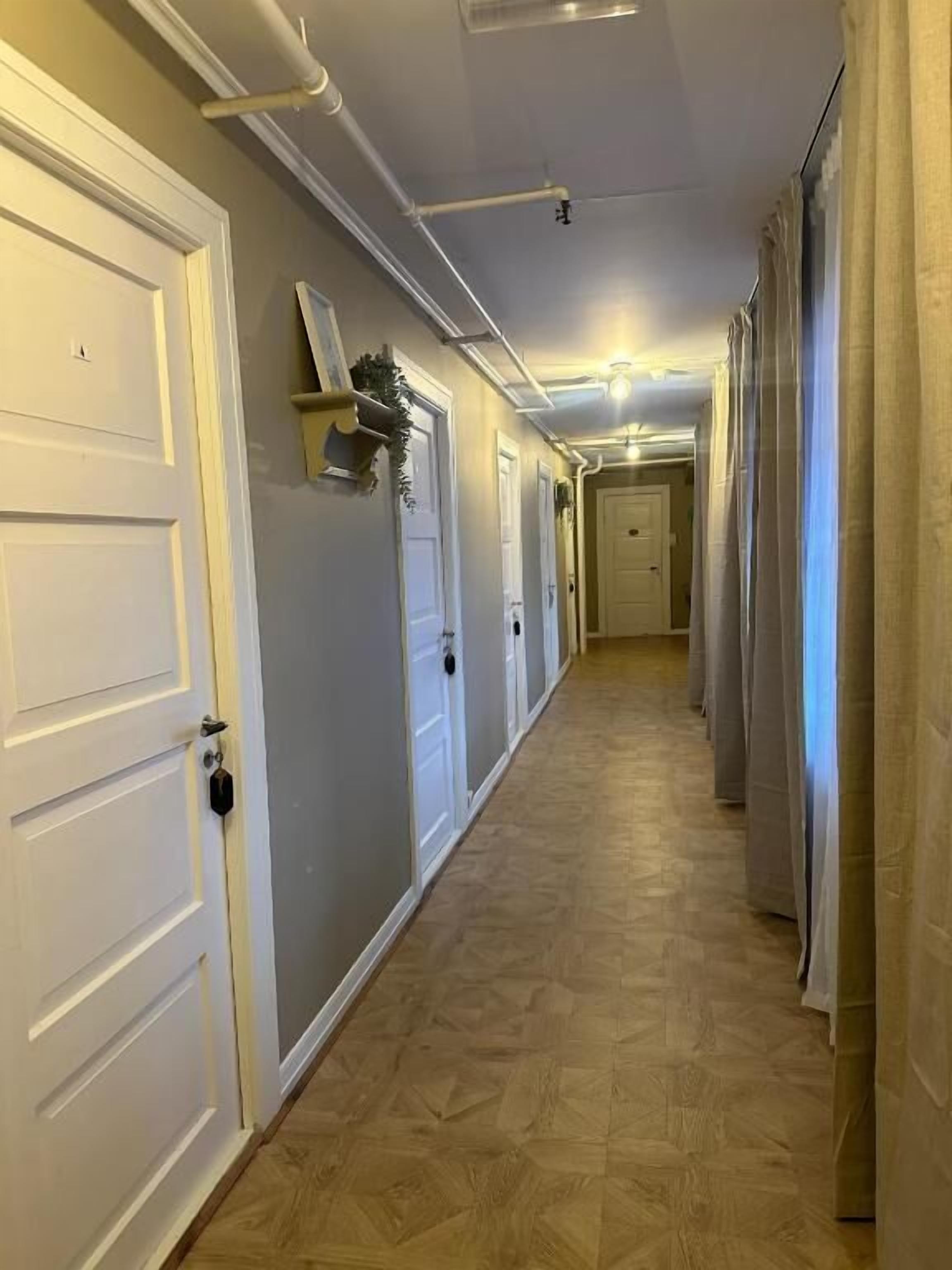 A hallway with white doors, a wooden floor, and a ceiling with exposed pipes and a light fixture.