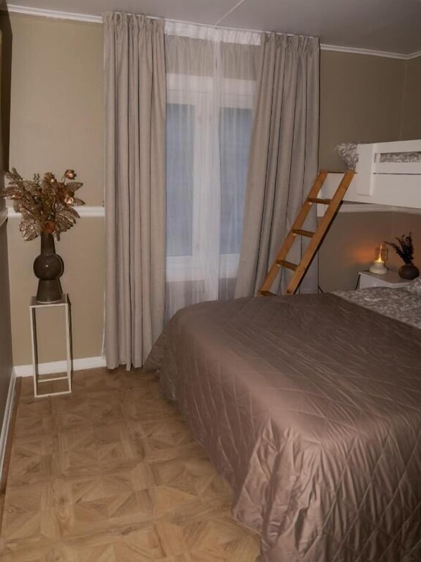 A bedroom with a bed, a window with curtains, a bedside table with a lamp, and a wooden ladder leaning against the wall. - Huset Vårt Bed and Breakfast (Volda)