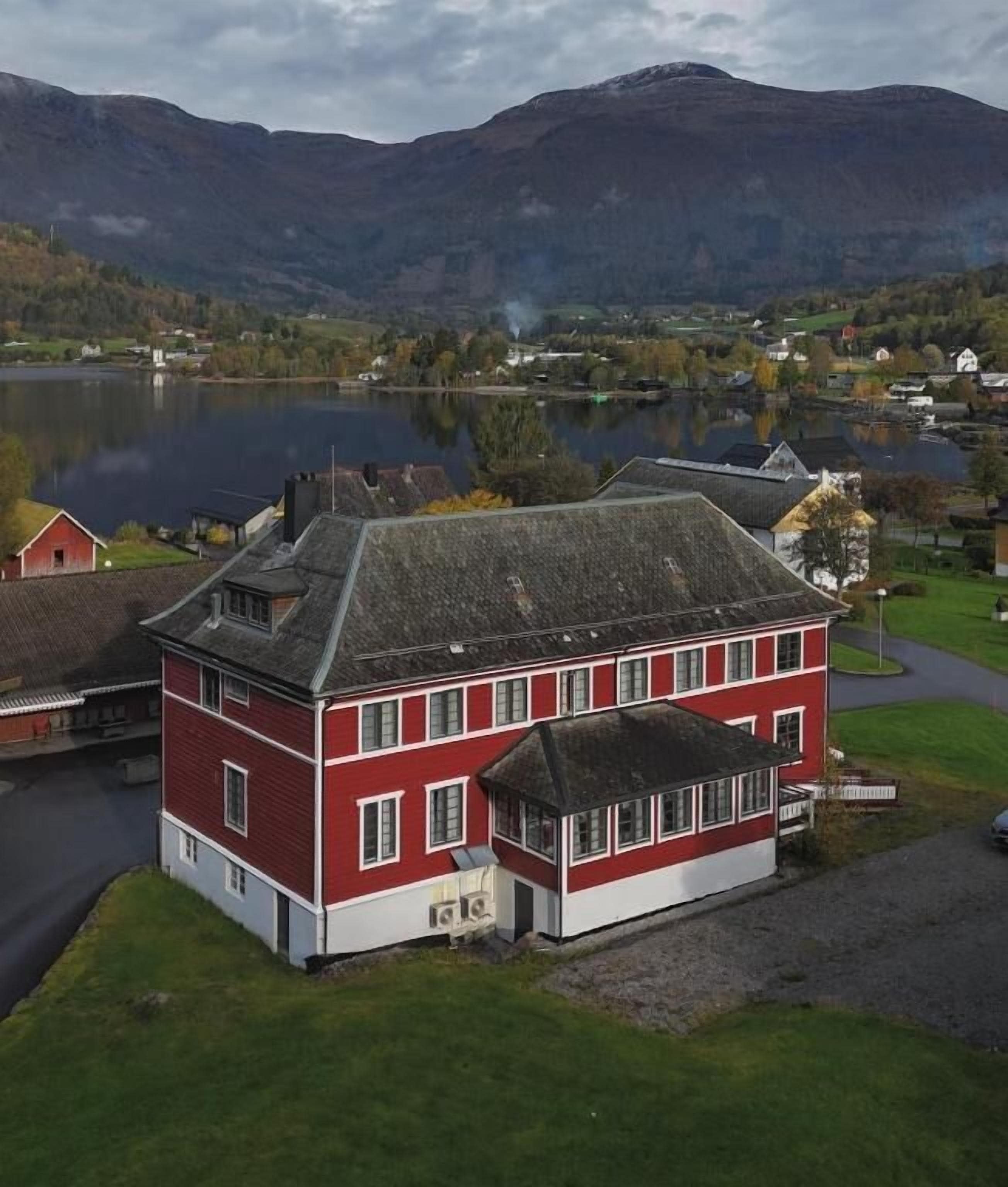 En röd och vit byggnad med ett brant tak, omgiven av en sjö och berg.