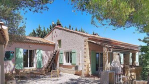 A rustic stone building with a tiled roof, a staircase leading to a door, and a small outdoor seating area with wooden furniture. - House in Aramon, a pretty village in the Gard, in the hills overlooking the Rhone (Aramon)