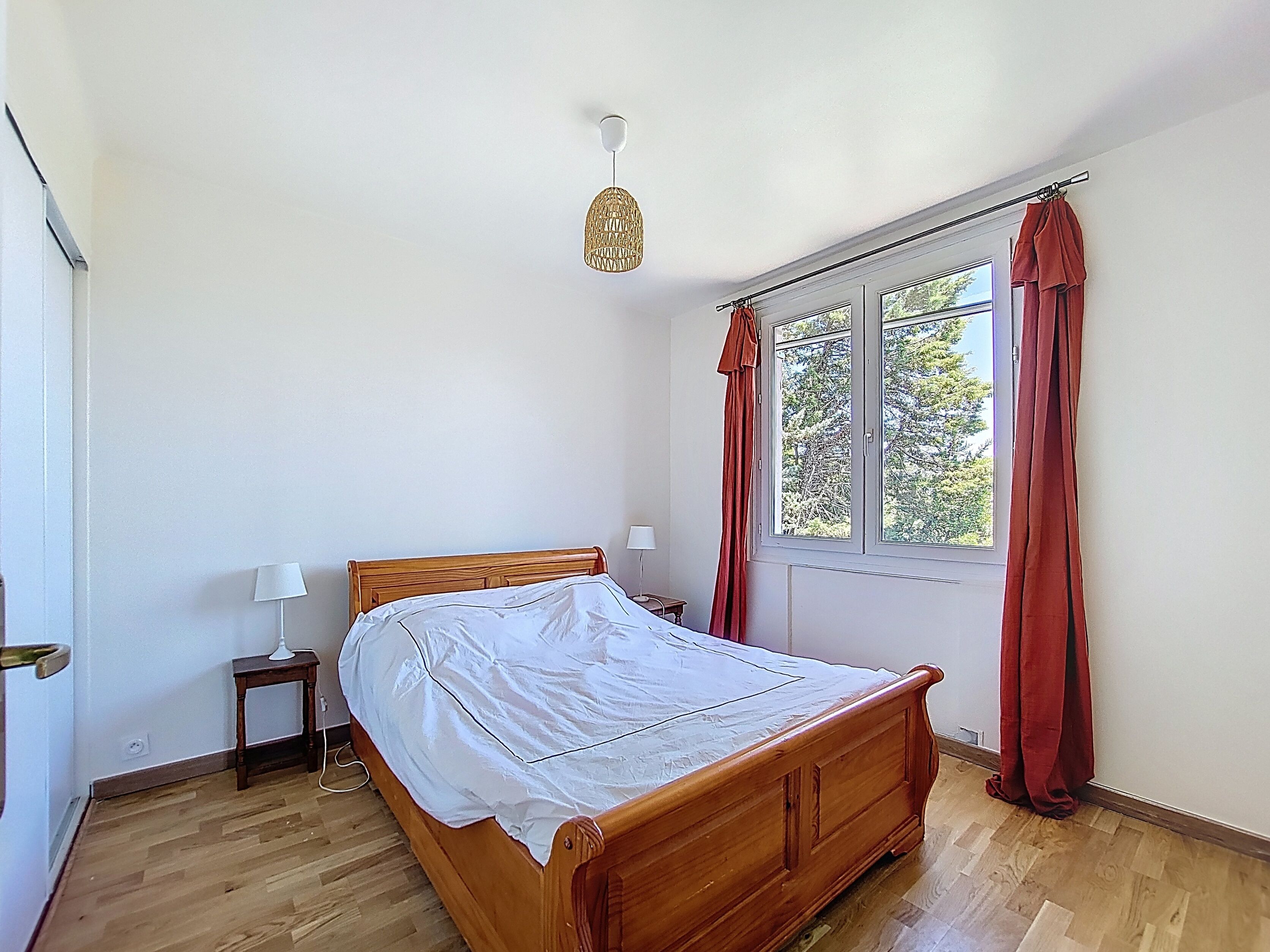 Una camera da letto con un letto in legno, un comodino con una lampada, una finestra con tende e un lampadario.