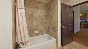 Une salle de bain équipée d’une baignoire, d’une douche et d’une porte donnant sur un espace cuisine.
