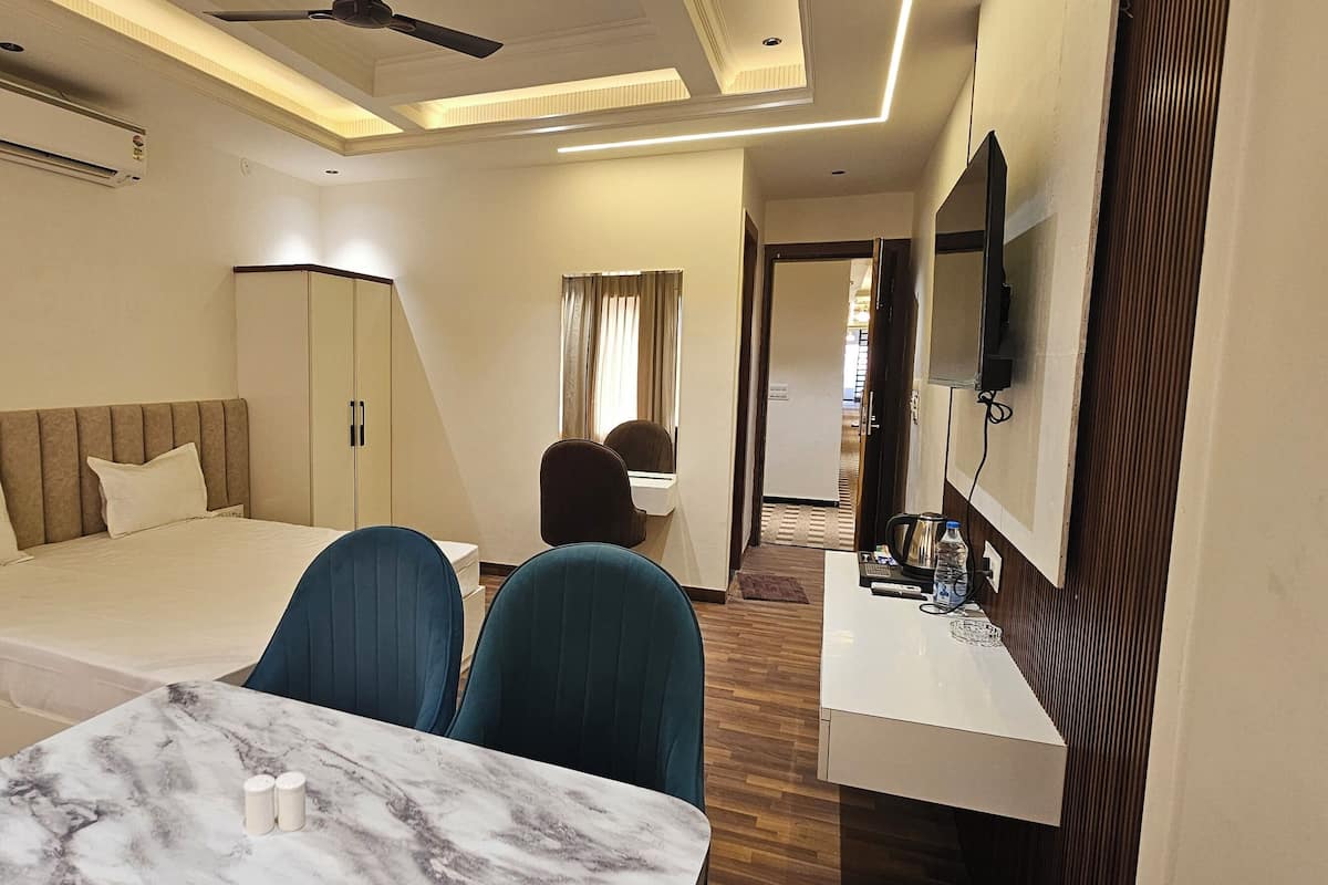 A hotel room with a bed, a desk, a chair, a table, a mirror, and a ceiling fan.