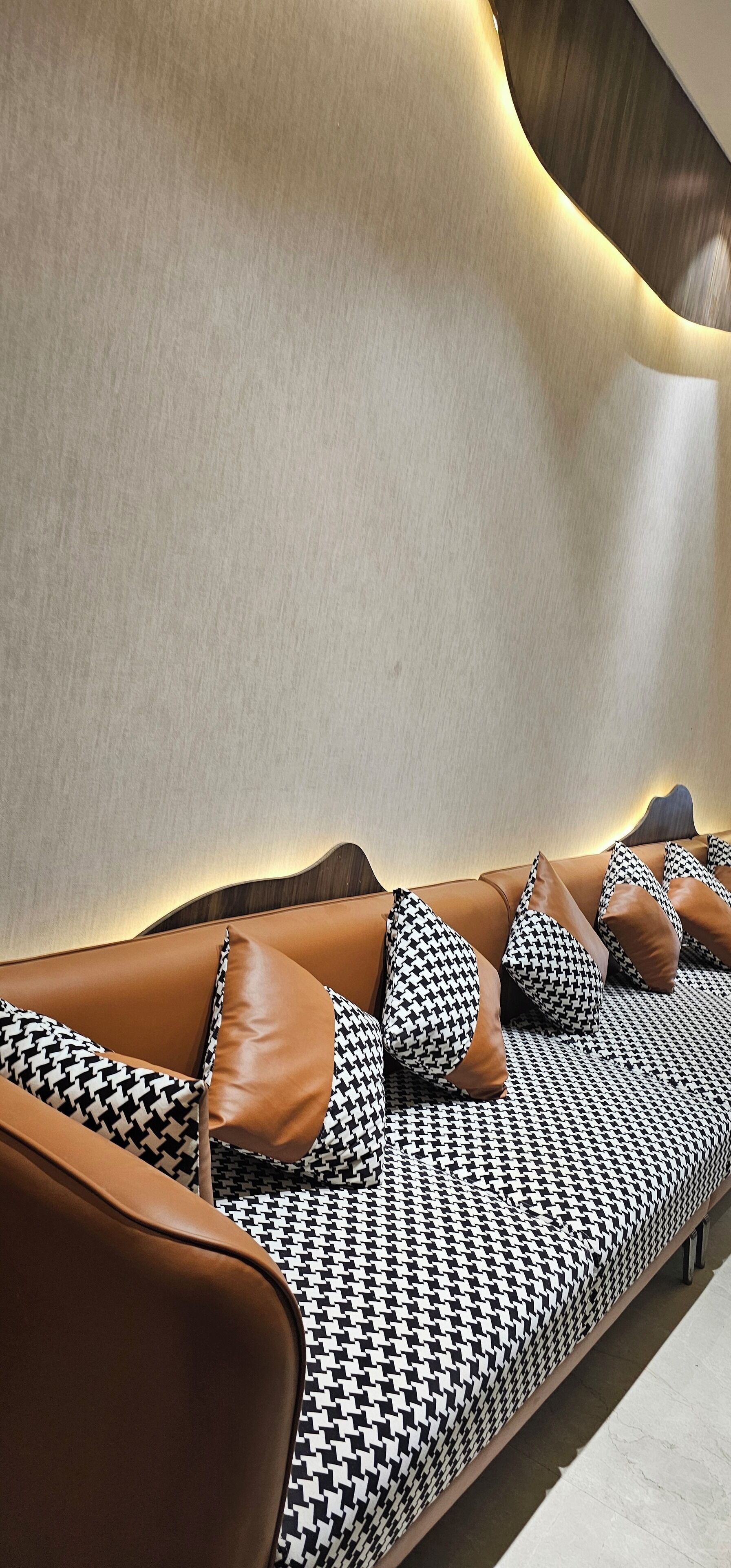 A modern sofa with a houndstooth pattern and brown leather cushions, positioned against a wall with a wooden finish.