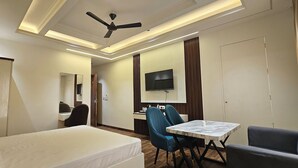 A hotel room with a bed, a desk, a chair, a TV, and a ceiling fan. - Hotel Sharanga (Hisar)