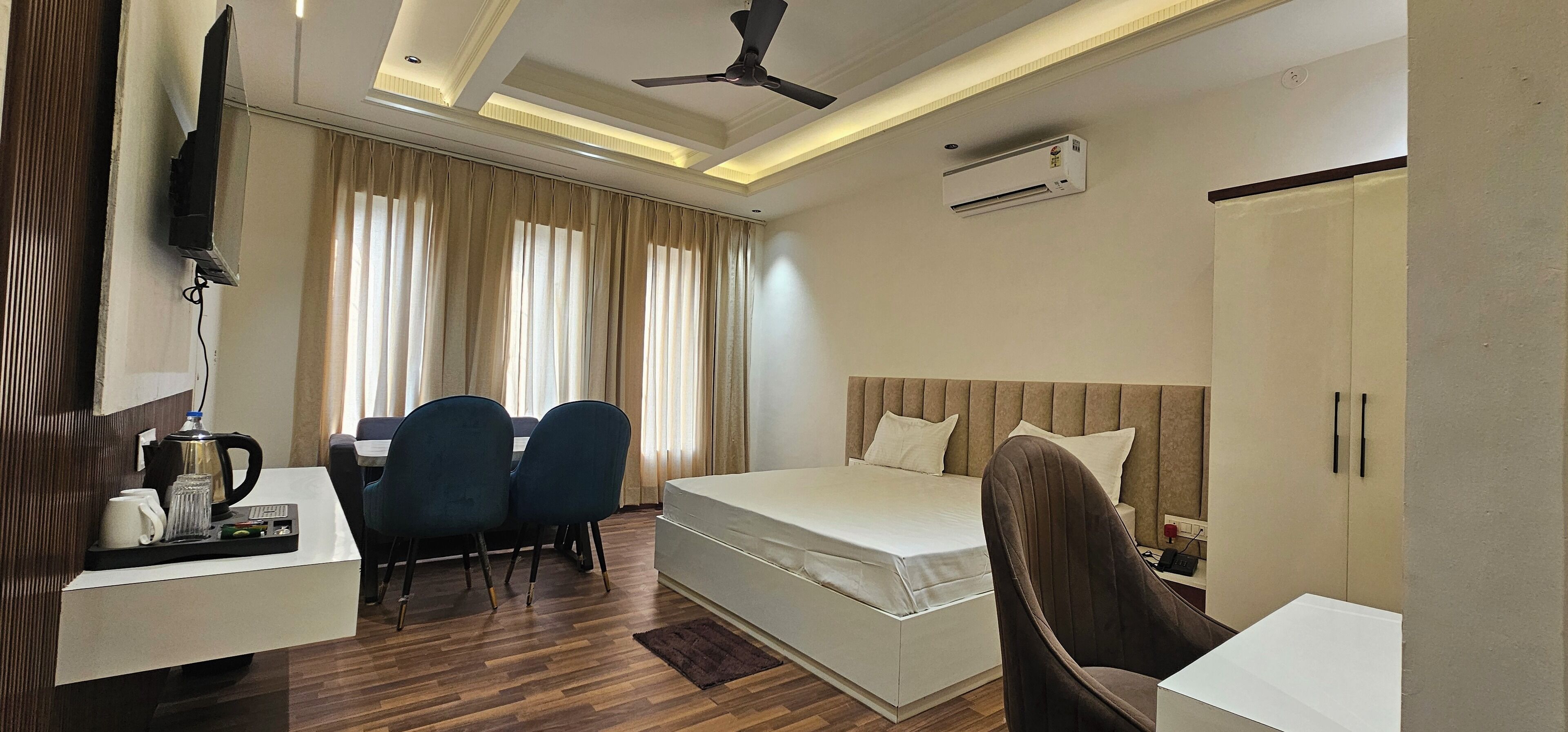 Een hotelkamer met een bed, een bureau met stoelen, een televisie, een airconditioning en een plafondventilator.