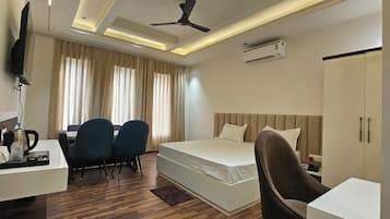 Een hotelkamer met een bed, een bureau met stoelen, een televisie, een airconditioning en een plafondventilator.