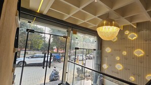 A hotel lobby with a large chandelier, a glass entrance, and a decorative wall with floral patterns. - Hotel Sharanga (Hisar)