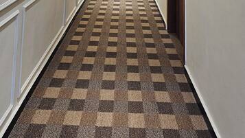 A hotel hallway with a checkered carpet, recessed lighting, and wall sconces.