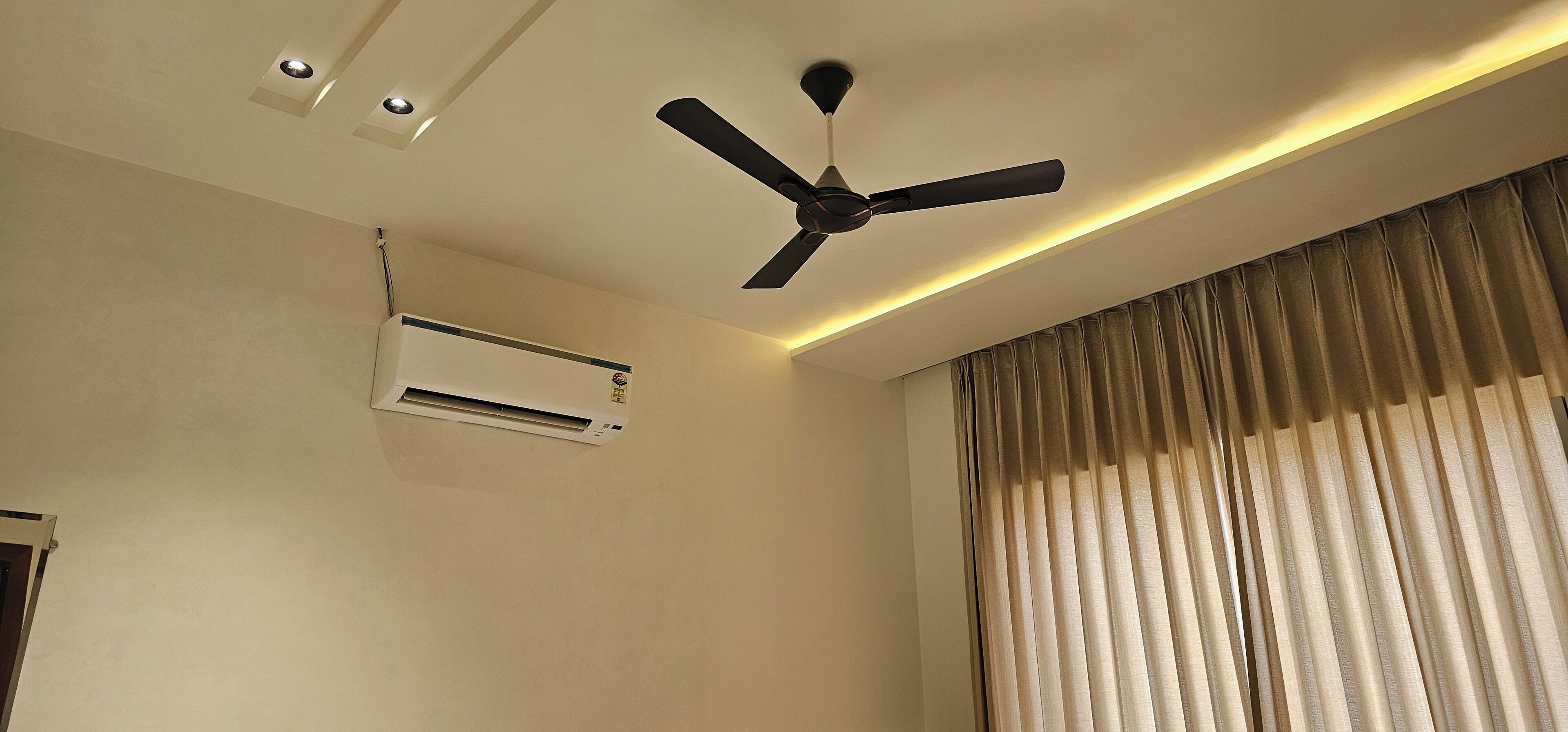 A room with a ceiling fan, an air conditioning unit, and a large window with curtains.