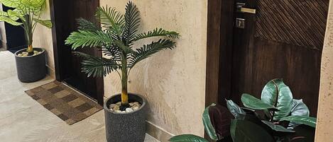 A hallway with two doors labeled "Restroom" and "SHE," each with a corresponding restroom symbol. There are potted plants along the hallway.