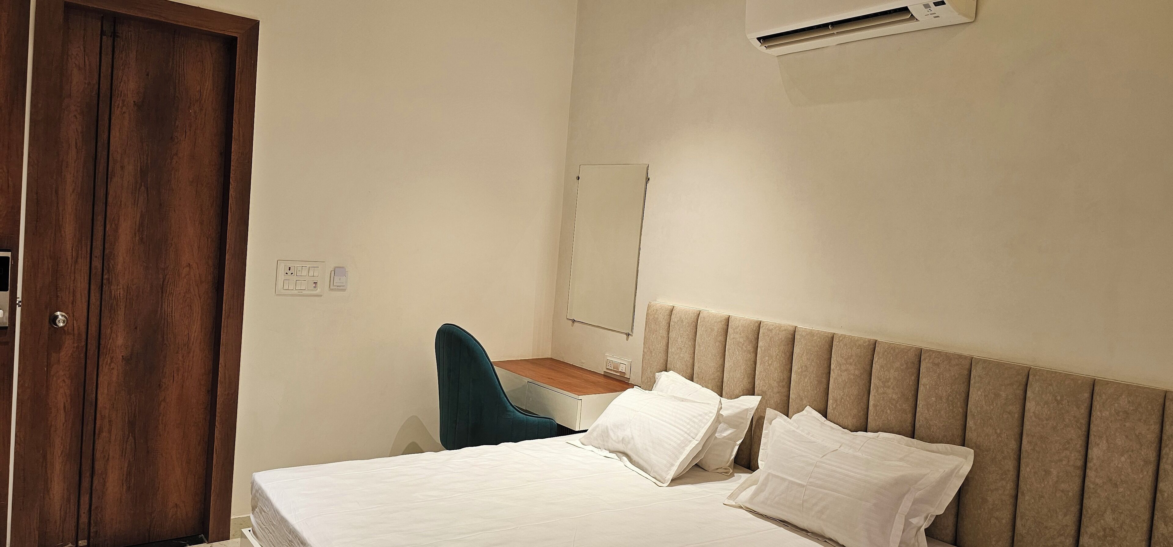 A bedroom with a bed, a desk, a chair, and a mirror.
