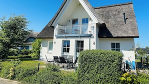 A two-story house with a balcony, white exterior, and a thatched roof. - Reethaus Arkonablick - Villa by the sea with fenced garden. Dogs welcome. (Glowe)