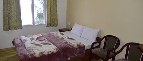 A bedroom with a bed, two chairs, a window with curtains, and a wooden floor.