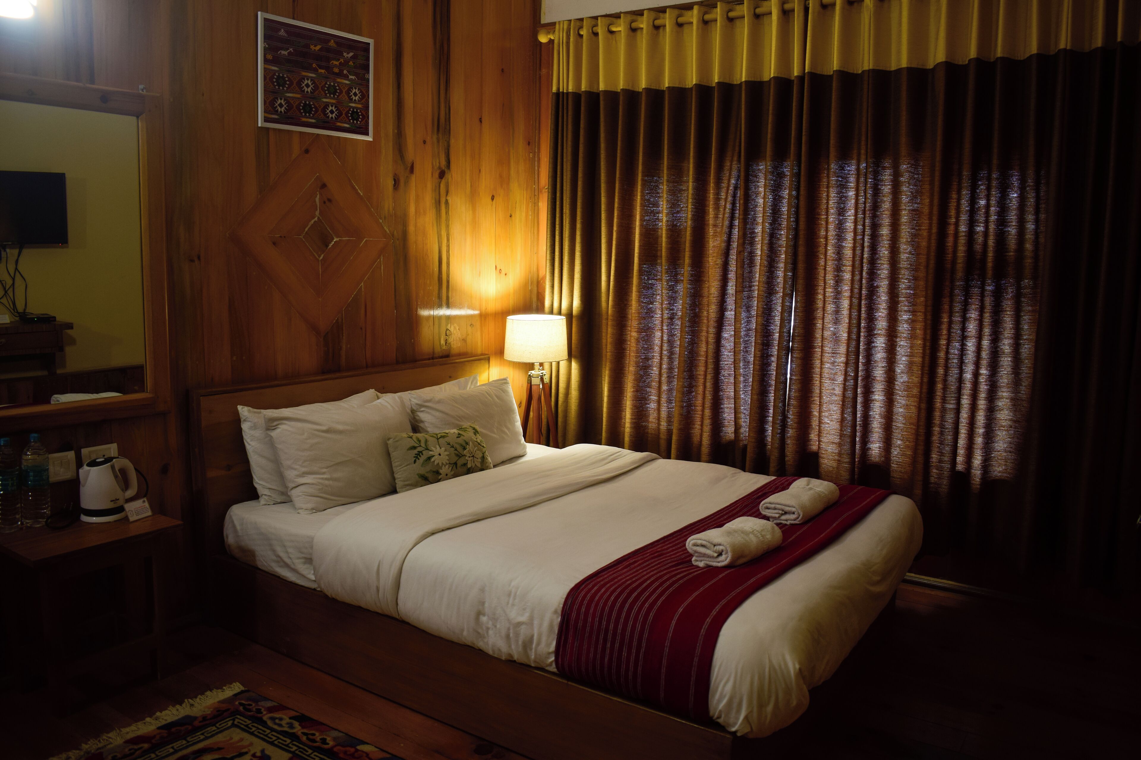 A neatly made bed with a red blanket, a bedside lamp, and a wooden headboard.
