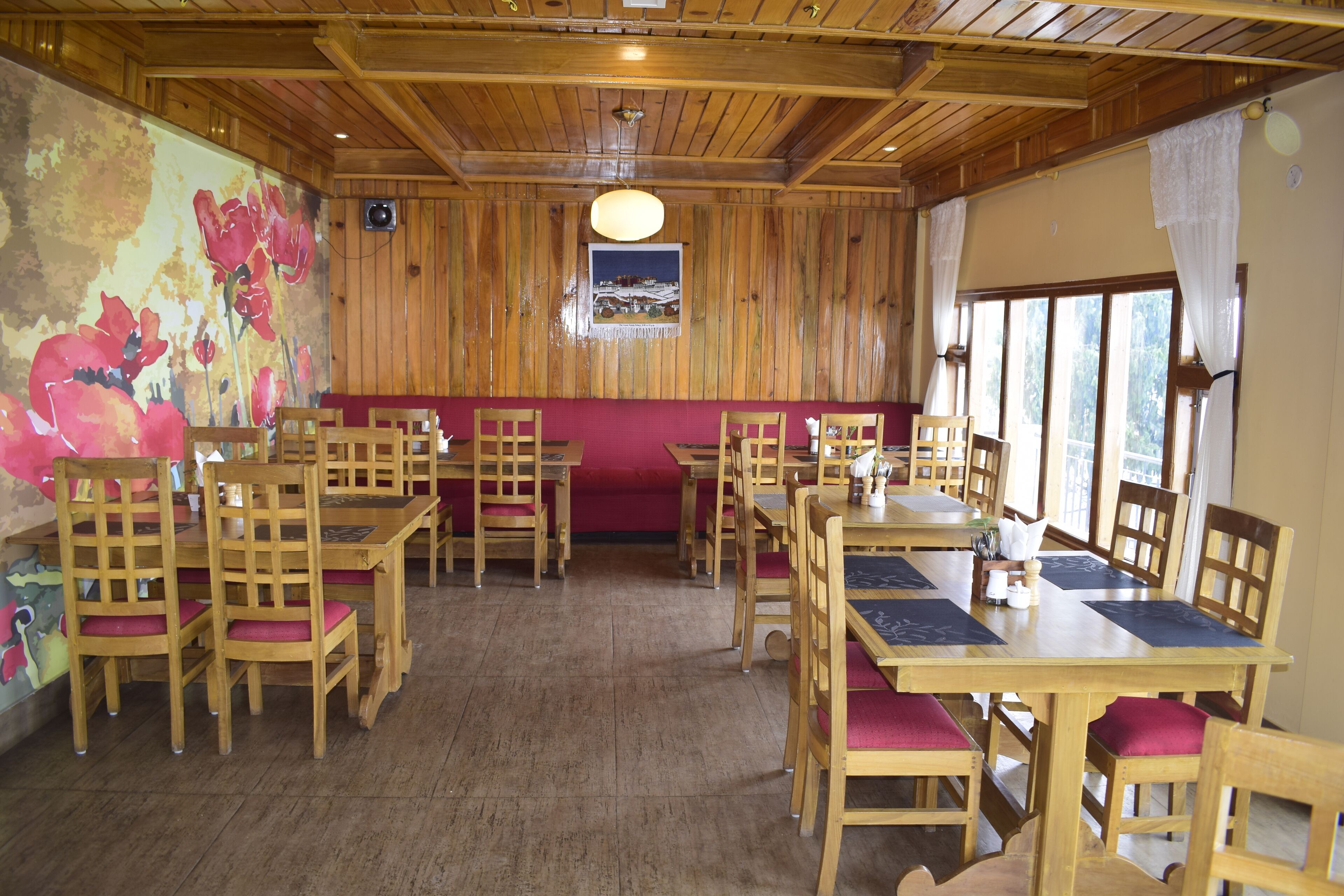 A restaurant with wooden tables and chairs, a mural on the wall, and a window with curtains.