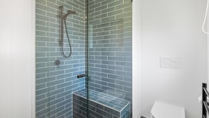 Ein modernes Badezimmer mit einer Duschkabine, einer weißen Toilette und einer gefliesten Wand.