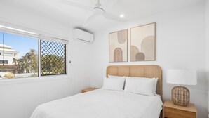 Ein Schlafzimmer mit einem großen Bett, einem Deckenventilator, einem Fenster mit Aussicht und zwei an der Wand befestigten Kunstwerken.